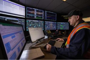 A man monitors multiple control screens in an industrial control room.