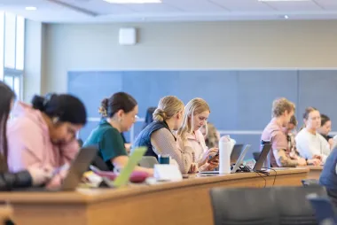 Students seated in a classroom using laptops and taking notes.