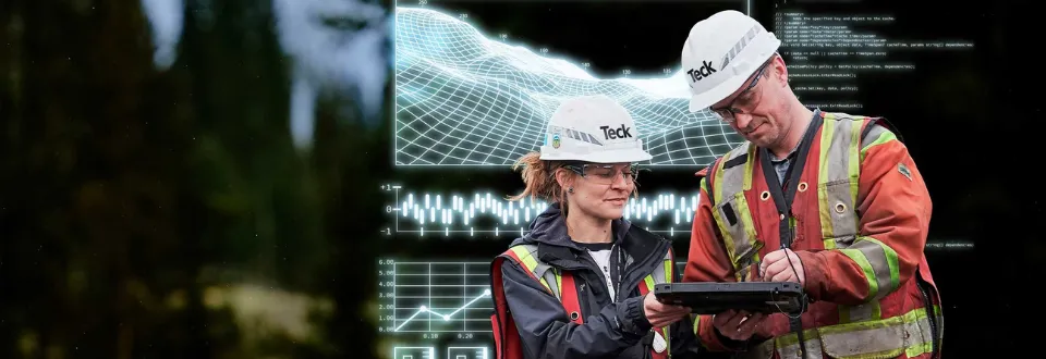 Two workers in safety gear reviewing data on a tablet.