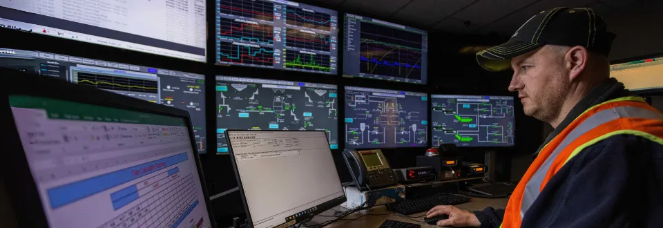 Worker monitors multiple control screens in an industrial control room.