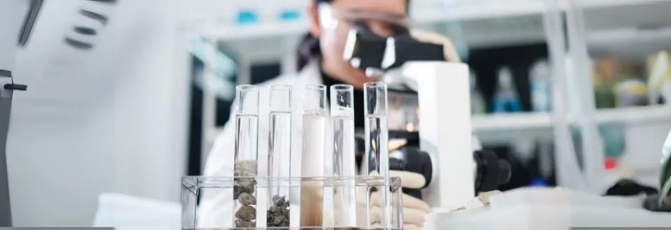 Lab samples in test tubes with a researcher looking in a microscope in the background